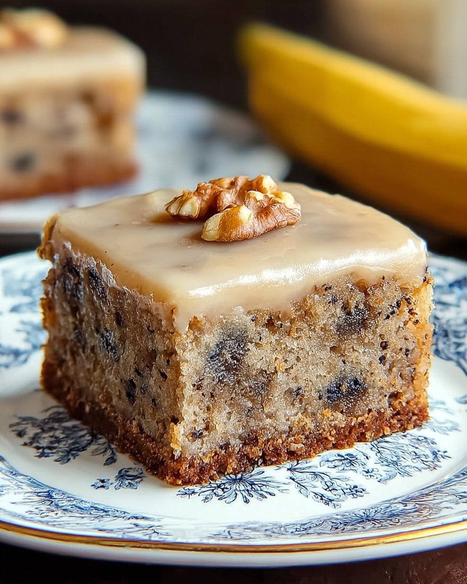 A thick square piece of moist banana cake with dark brown spots of banana bits inside, sitting on a white plate with a detailed blue floral pattern. The cake shows two layers: the bottom layer is a darker brown crust, and the main body is a light tan with visible specks and chunks. The top layer is a smooth, light beige glaze with a few walnut pieces embedded. The background is softly blurred with a banana and another banana cake slice visible. photo taken with an iphone --ar 4:5 --v 7