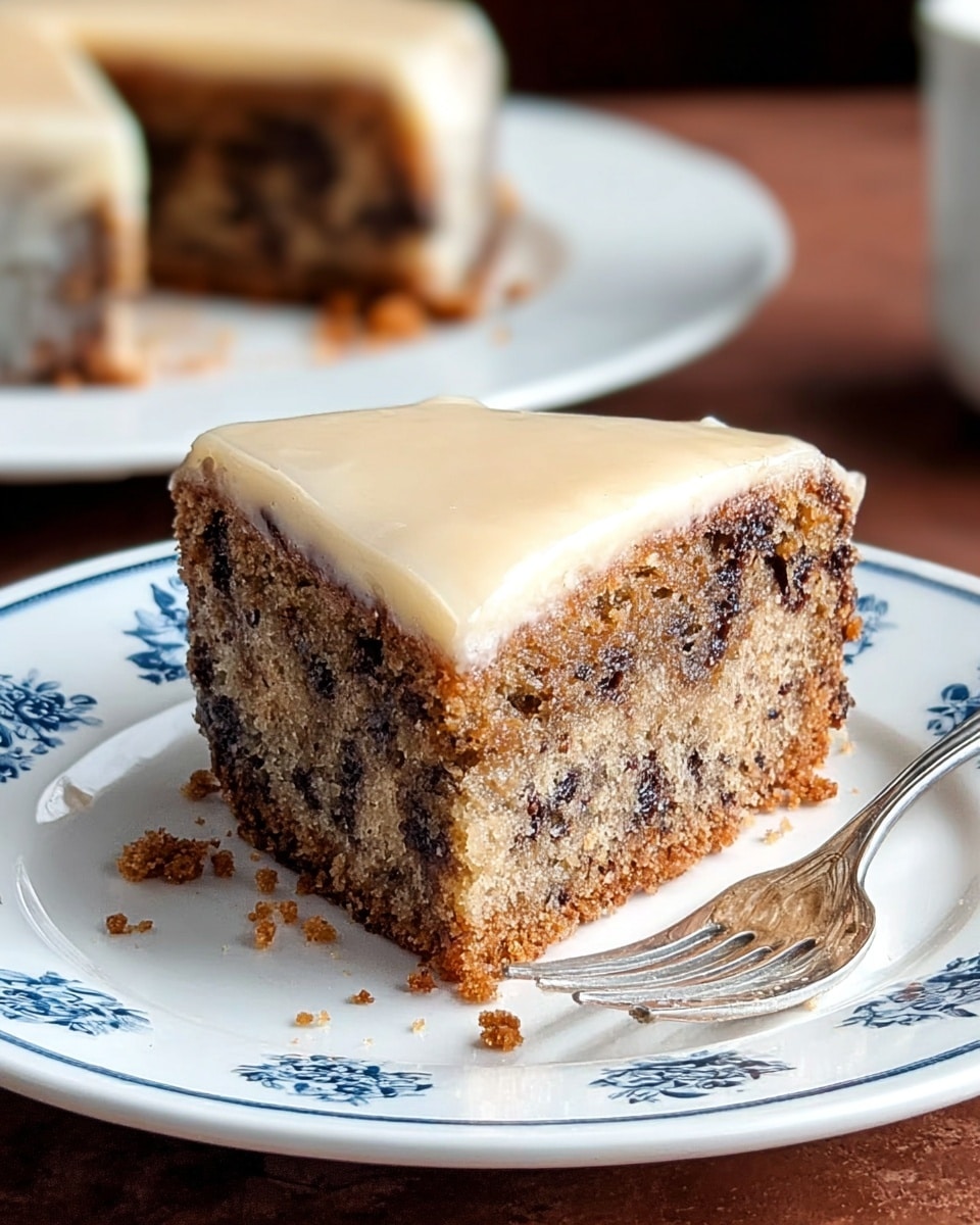 A single slice of cake sits on a white plate with blue floral patterns, showing two main layers: a thick, moist bottom layer with a mix of light brown and dark chocolate chips, and a smooth, light cream-colored layer on top that looks like a glaze or icing. The cake slice has a crumbly texture around the edges, and some crumbs have fallen onto the plate. In the background, there is a blurred image of the whole cake on a white plate, with a missing slice where this piece came from. A silver fork rests next to the slice on the plate, all placed on a brown surface replaced by a white marbled texture. photo taken with an iphone --ar 4:5 --v 7