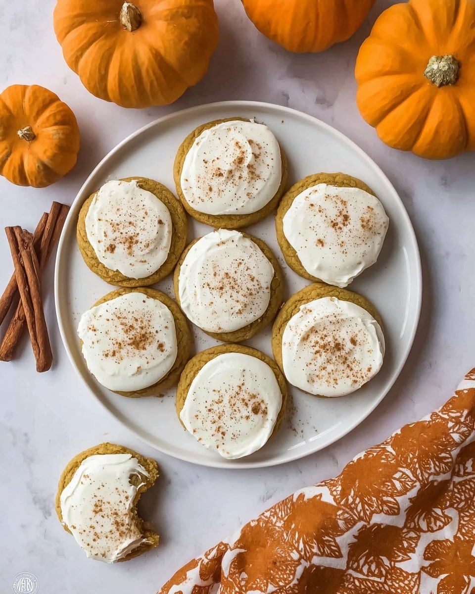 A white round plate holds seven golden brown cookies, each topped with a smooth, thick layer of white frosting sprinkled with light brown cinnamon powder. Around the plate, there are two whole bright orange pumpkins and two cinnamon sticks placed on a white marbled surface. In the bottom left corner, there is a partially eaten cookie with the same frosting. On the right side, part of an orange fabric with autumn leaf patterns is visible. The image has a warm, cozy feel. photo taken with an iphone --ar 4:5 --v 7