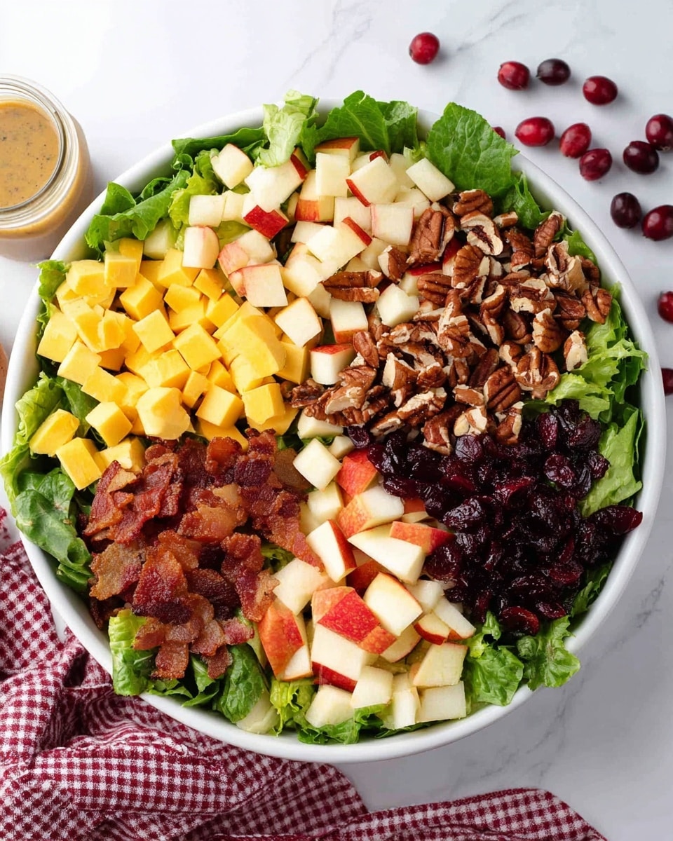A white bowl filled with a fresh salad showing five main layers. The bottom layer is made of bright green leafy lettuce covering the whole bowl. On top, starting from the left side moving clockwise, there is a neat pile of small, yellow cheese cubes, followed by a cluster of rich brown, chopped pecans with a rough texture. Next to the pecans, there is a group of white and red-skinned apple pieces, cut into small, bite-sized chunks. Below the apples, there are crispy, golden-brown bacon bits, and lastly, dark red dried cranberries with a wrinkled texture fill the last section. The bowl rests on a white marbled surface with a small jar of dressing and a woman’s hand partially visible at the corner holding a cloth with red checkered pattern. Some dried cranberries are scattered on the surface. Photo taken with an iphone --ar 4:5 --v 7