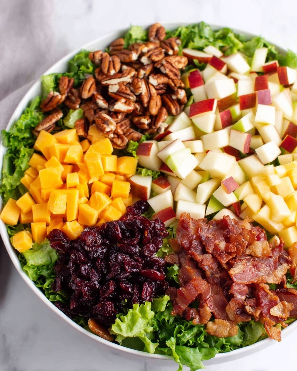 A white bowl filled with a fresh salad showing five layers of ingredients neatly arranged on a bed of chopped green lettuce. Starting from the back left, the first layer is made of toasted brown pecan pieces, next to it diced pear chunks with white inside and red skin, then towards the front right, crispy bits of cooked bacon with a golden-brown color. On the front left side, small cubes of bright yellow cheddar cheese are seen, next to it dark red dried cranberries with a wrinkled texture. The bowl rests on a white marbled surface. photo taken with an iphone --ar 4:5 --v 7