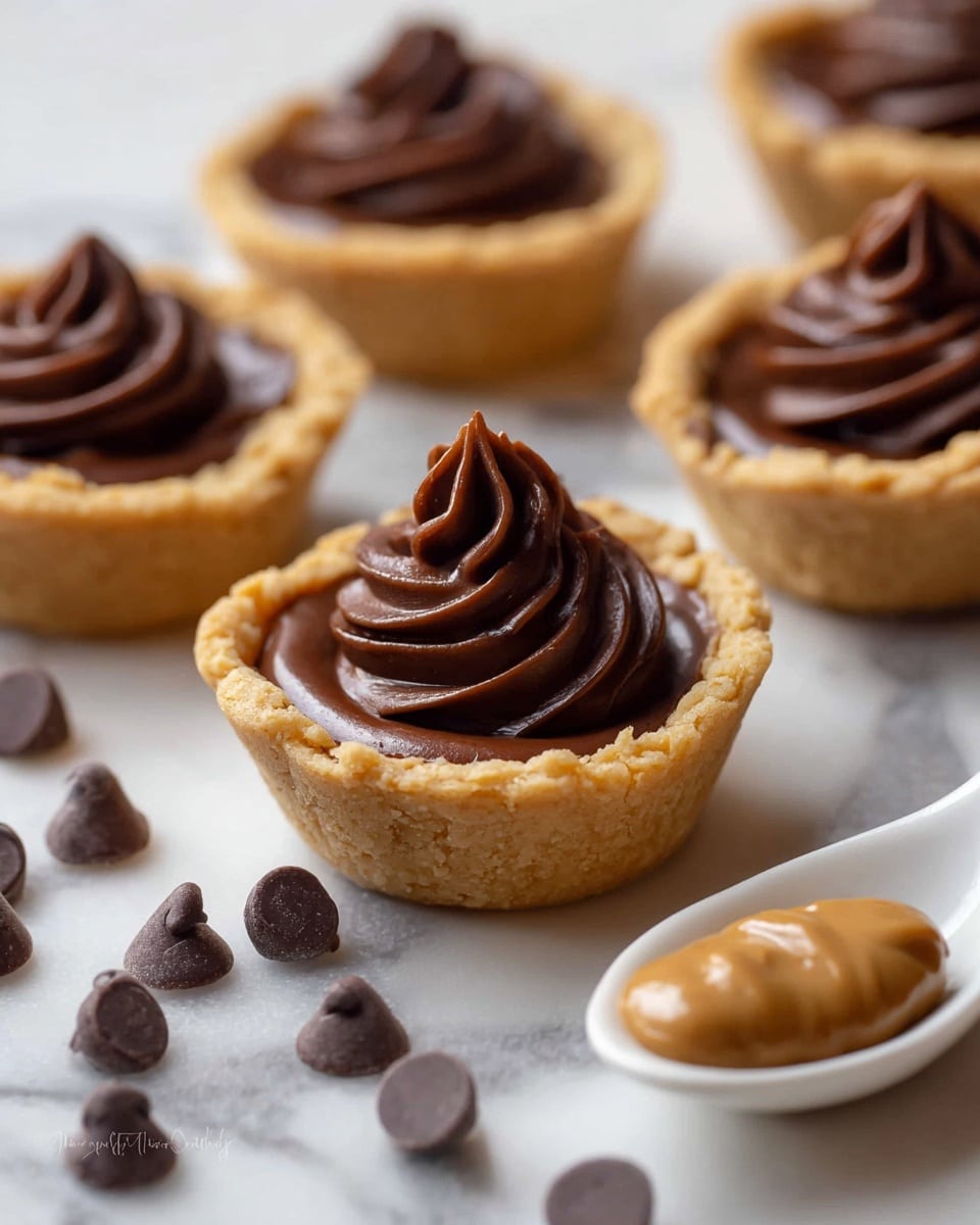 The image shows a white plate holding fifteen small cookie cups filled with smooth, shiny dark chocolate ganache. Each cookie cup has a light golden-brown, crumbly crust that forms the base and sides, with the dark chocolate filling swirled thickly inside, rising slightly above the crust edges with soft peaks. The plate is set on a white marbled surface, and the cookie cups are arranged closely together in a loose grid pattern, giving a neat, inviting look. photo taken with an iphone --ar 4:5 --v 7