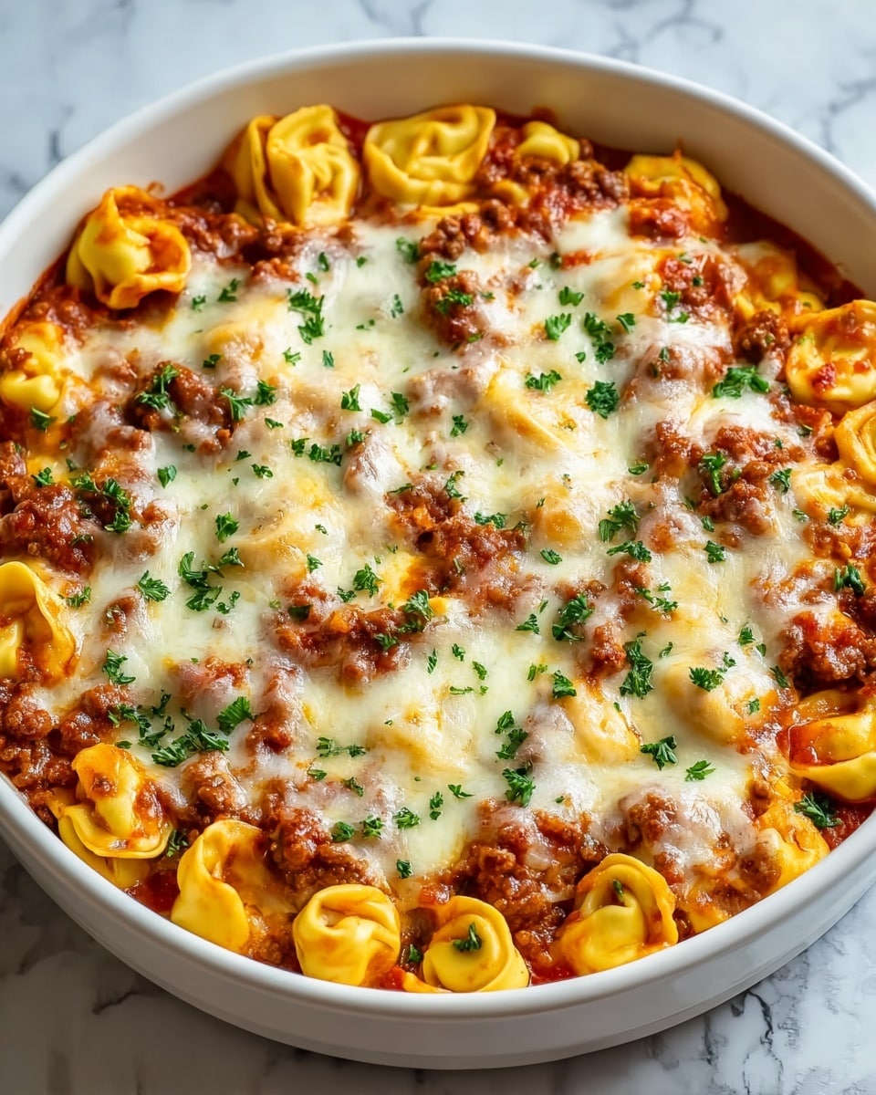 A white round casserole dish filled with a baked tortellini pasta layered with a rich red tomato sauce mixed with ground meat, topped with a thick layer of melted and slightly browned cheese. The cheese is creamy white with golden brown spots, and the dish is sprinkled with small pieces of green parsley evenly scattered on top. The tortellini pasta is yellow and appears soft and plump, peeking through the sauce and cheese layers. The dish sits on a white marbled textured surface, giving it a fresh, clean background. photo taken with an iphone --ar 4:5 --v 7