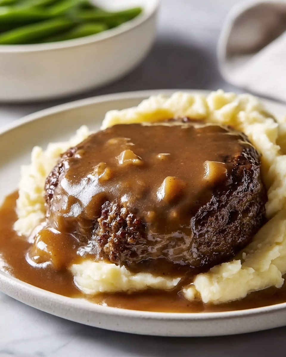 A round white plate holds a dish with two main layers. The bottom layer is a thick, dark brown, slightly chunky gravy spread across the plate, pooling around the edges. On top of the gravy is a thick, crispy-edged ground beef patty, dark brown and textured. The patty is generously covered with more gravy, which is glossy and smooth with visible black pepper specks. Behind the patty, there is a large serving of creamy mashed potatoes that are soft and light beige, topped with small green herb bits. The whole scene is set on a white marbled surface. Photo taken with an iphone --ar 4:5 --v 7