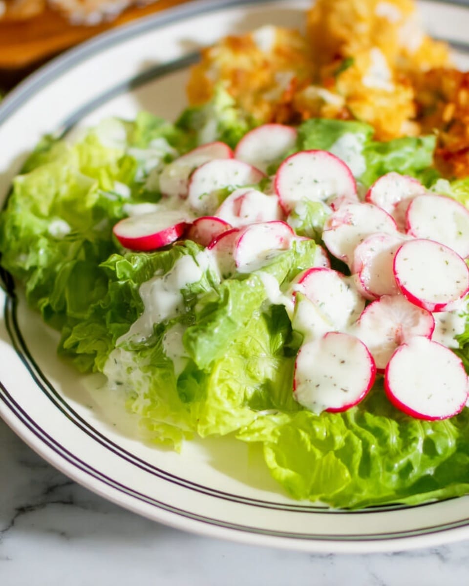 A close-up image of a fresh salad on a white plate with black thin stripes near the edge, placed on a white marbled surface. The salad has two main layers: the bottom layer with large, bright green lettuce leaves creating a base, and the top layer with thinly sliced radishes showing white centers and red edges scattered evenly. White creamy dressing is drizzled generously over the salad, covering parts of the lettuce and radishes. In the background, there are some pieces of golden-brown crispy food, slightly out of focus. photo taken with an iphone --ar 4:5 --v 7