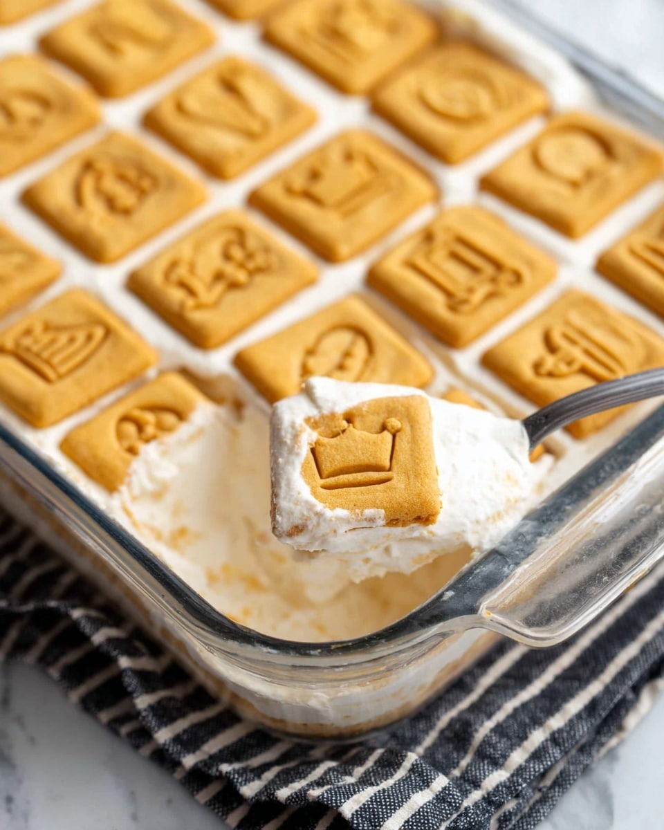 The image shows a square-shaped dessert on a white plate with three visible layers. The bottom layer is made of pale yellow banana slices arranged neatly on a light-colored cookie base. The middle layer is thick and fluffy, white cream with a soft texture, covering the bananas fully. The top layer consists of two square light brown cookies with a slightly darker pattern imprinted, placed side by side. The dessert appears creamy and soft, with a bite taken out of the front left corner, revealing the layers clearly. In the background, whole bananas and a glass of milk are slightly out of focus on a white marbled surface. A wooden fork rests near the plate. Photo taken with an iphone --ar 4:5 --v 7