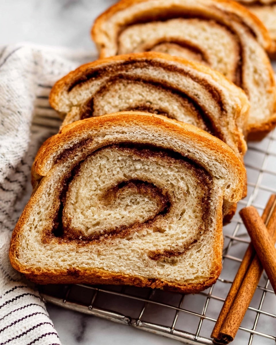 Three slices of cinnamon swirl bread are shown on a silver cooling rack with a white marbled surface underneath. Each slice has several layers: a light brown outer crust, soft tan bread with a spongy texture, and a spiral of darker brown cinnamon filling running through the middle. Two cinnamon sticks lie next to the slices on a white fabric with thin black stripes. The picture is a close-up, highlighting the bread’s fluffy texture and the cinnamon swirl’s deep color. Photo taken with an iphone --ar 4:5 --v 7