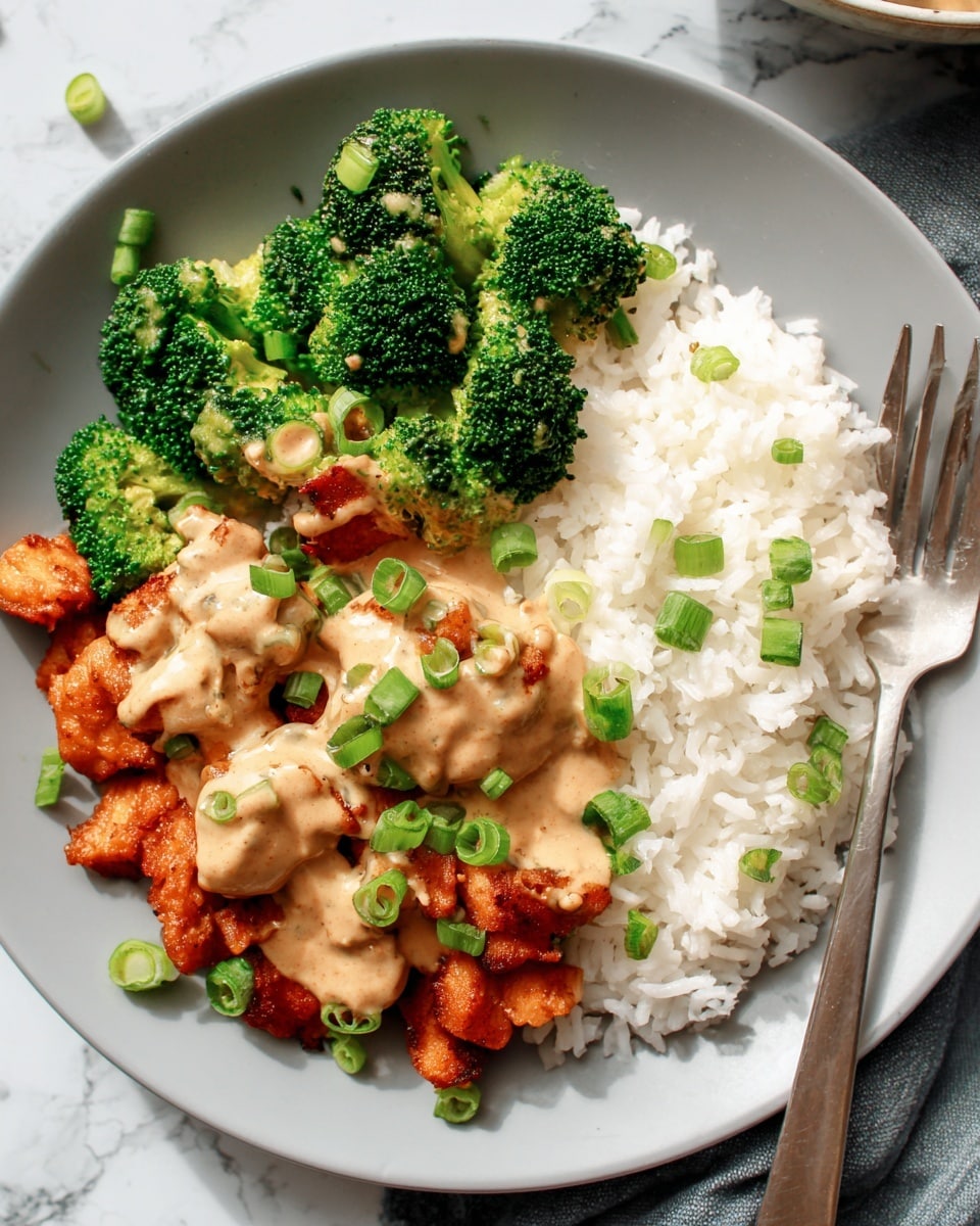 On a white plate, there is a serving of white rice on the right side with soft, separate grains. To the left of the rice, there is bright green broccoli with tight florets, topped with light brown sauce drizzled unevenly over it. In front of and partially on top of the rice, there are small pieces of reddish-brown cooked chicken that look crispy, covered with more of the creamy light brown sauce. The dish is garnished with thinly sliced green onions scattered across the chicken and sauce. The plate is set on a white marbled surface with a silver fork resting on the right edge. Photo taken with an iphone --ar 4:5 --v 7