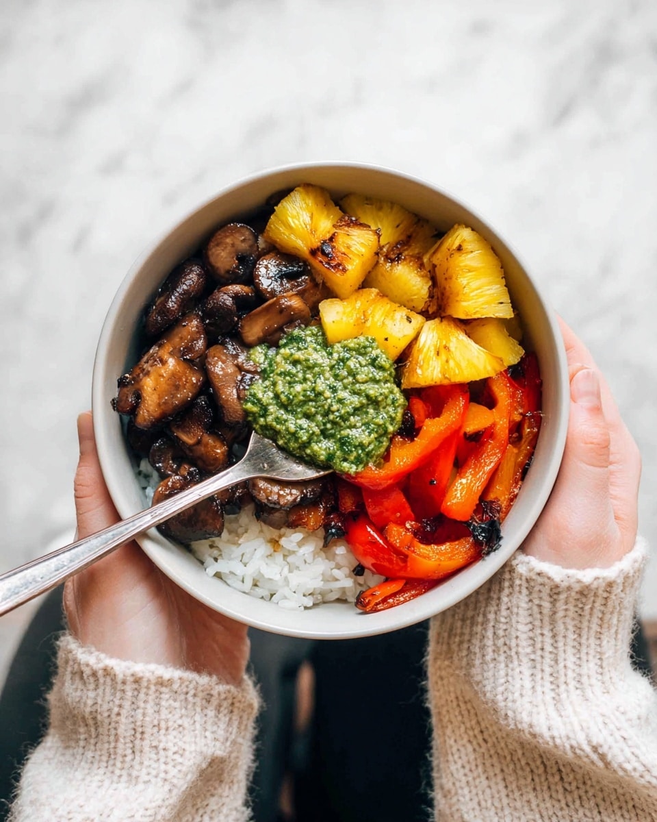 A bowl with four distinct layers is held by a woman's hand wearing a cream-colored knit sweater. The bottom layer is white rice, visible in small parts beneath the toppings. On one side, there are sautéed dark brown mushrooms with a slightly glossy texture. Next to the mushrooms, there are grilled yellow pineapple chunks with light brown grill marks, looking juicy. On the opposite side from the mushrooms, there are roasted red and yellow bell pepper strips, soft and shiny. In the center sits a bright green, coarse-textured pesto sauce. A silver spoon is resting inside the bowl, touching the mushrooms. The bowl is white on the inside and has a smooth finish, set against a white marbled background. photo taken with an iphone --ar 4:5 --v 7