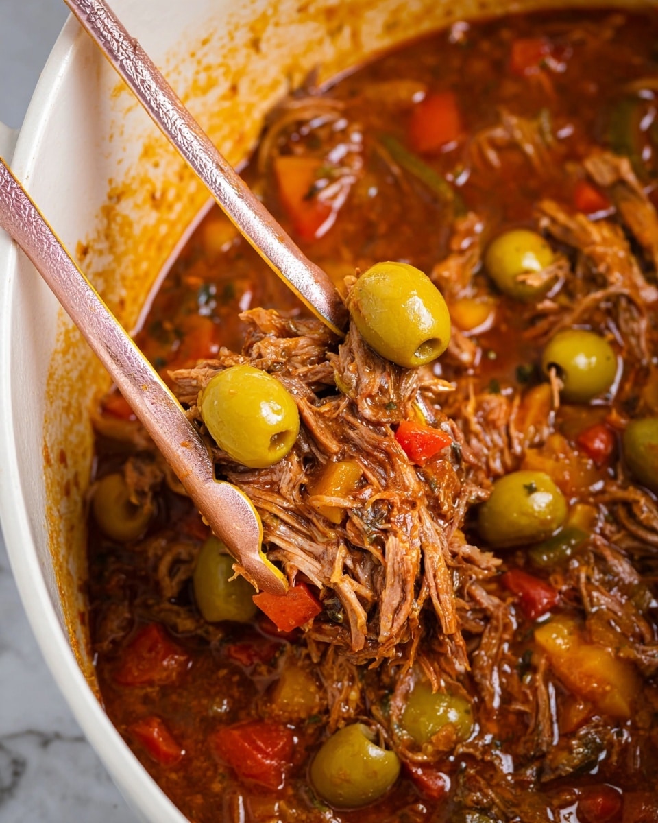 A close-up view of a stew with shredded meat mixed with whole green olives, diced red and yellow peppers, and other small vegetables in a rich, thick reddish-brown sauce. Two pink and gold kitchen tongs hold some of the stew above the pot’s white interior, showing the fibrous texture of the meat and the glossy surface of the olives and vegetables, all resting on a white marbled texture surface. photo taken with an iphone --ar 4:5 --v 7