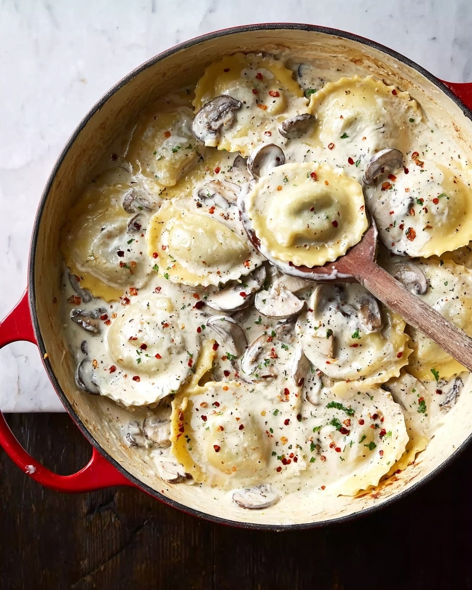 A large red cast iron pan placed on a white marbled surface is filled with several round ravioli pasta pieces, each layered flat and slightly overlapping. The ravioli are coated in a thick creamy white sauce with visible slices of light brown mushrooms and specks of black pepper and red chili flakes scattered throughout. A wooden spoon rests in the pan, partially lifting some ravioli to reveal the sauce underneath. The edges of the pan show light browning and use marks, adding texture and warmth to the image. Photo taken with an iphone --ar 4:5 --v 7